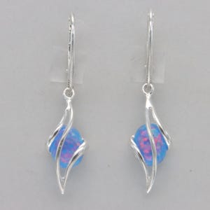 May include: A pair of silver dangle earrings with a blue opal stone set in a twisted wire design.