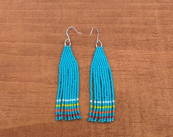 May include: A pair of turquoise beaded earrings with silver hooks. The earrings have a fringe of turquoise beads with a thin stripe of red, orange, yellow, and white beads.