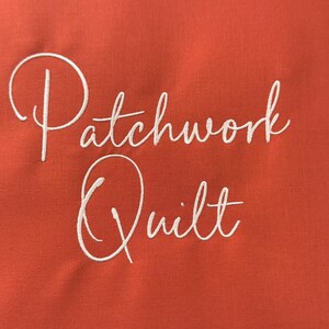 K&ouml;nnte beinhalten: Ein orangefarbener Stoffhintergrund mit den Worten "Patchwork Quilt" in wei&szlig;er Schreibschrift gestickt. Der Text ist zentriert und nimmt den gr&ouml;&szlig;ten Teil des Bildes ein.