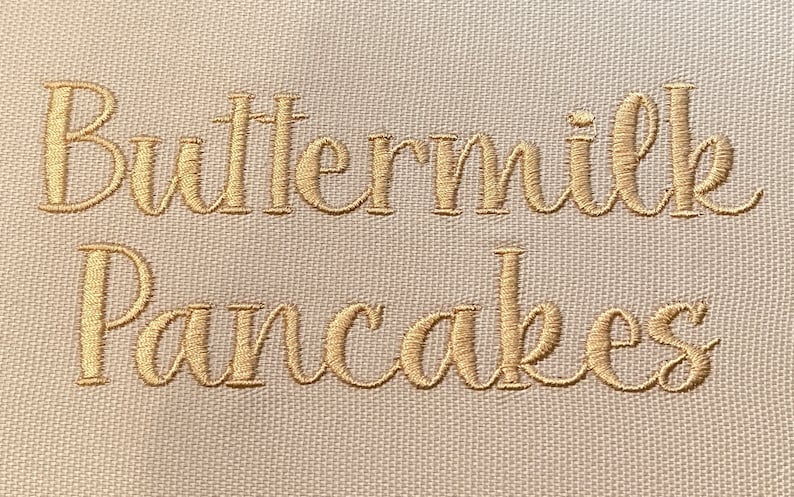 May include: A white kitchen towel with the words "Buttermilk Pancakes" embroidered in gold thread.