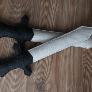 Könnte beinhalten: Zwei Filzschwerter, eines schwarz und eines weiß, liegen übereinander auf einer Holzoberfläche.