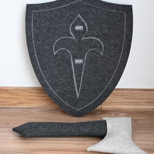 May include: A gray felt shield with a white fleur-de-lis design and a gray felt axe with a white felt blade.