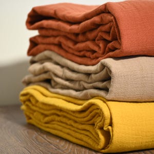 May include: A stack of folded fabric in shades of orange, tan, and yellow. The textiles appear to be made of a soft, textured material. The fabrics are neatly stacked, showcasing the different colors and textures.