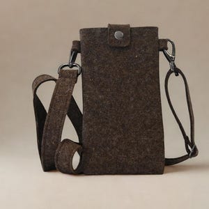 May include: A brown felt crossbody phone bag with a shoulder strap and a snap closure. The bag has silver-colored metal hardware and a simple, rectangular design. The strap is adjustable.