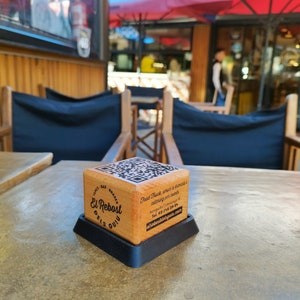 Puede incluir: Un bloque de madera con un código QR y el texto "El Rebost dels Guix" y la información de contacto de un camión de comida.