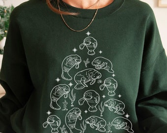 May include: A dark green sweatshirt featuring a white outline of a Christmas tree made of manatees. The tree is decorated with stars and the word "merry" is written at the bottom.
