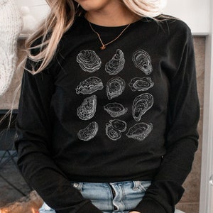May include: A black long-sleeved shirt with a white outline of various oyster shells printed on the front.