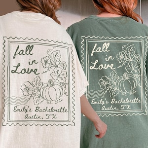 May include: Two t-shirts, one cream and one sage green, featuring a back graphic of a postage stamp design. The print includes a pumpkin, vine leaves, and the text "fall in Love", "est. 2026", and "Emily's Bachelorette Austin, TX" in a dark ink.