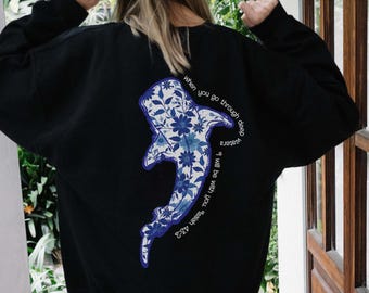 May include: Black sweatshirt with a blue and white whale graphic on the back. The whale has floral designs and the text "When you go through deep waters I will be with you" is printed around the whale.