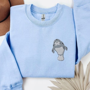 May include: Light blue sweatshirt with a gray embroidered manatee design.