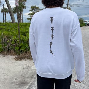 May include: White long-sleeve sweatshirt with a graphic of a line of hammerhead sharks printed on the back.