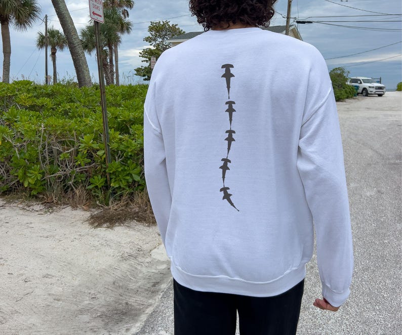May include: White long-sleeve sweatshirt with a graphic of a line of hammerhead sharks printed on the back.