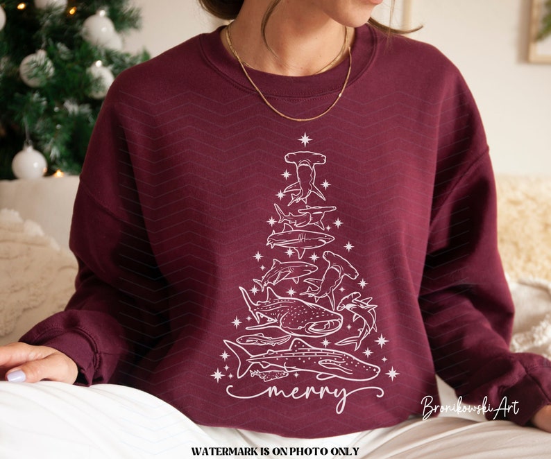 K&ouml;nnte beinhalten: Burgunderfarbenes Sweatshirt mit einer wei&szlig;en Grafik eines Weihnachtsbaums, der aus verschiedenen Haiarten besteht. Das Wort "merry" ist unten in Schreibschrift geschrieben. Das Design beinhaltet Sterne und einen Stern an der Spitze des Baumes.