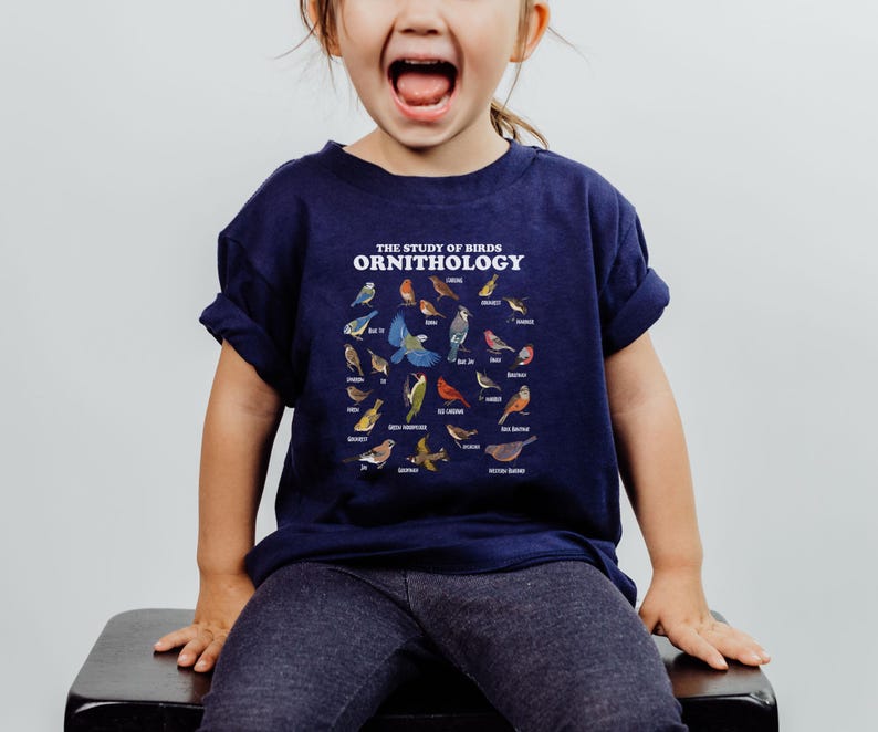 May include: A young child wearing a navy blue t-shirt with a white graphic of various birds and the text "THE STUDY OF BIRDS ORNITHOLOGY".