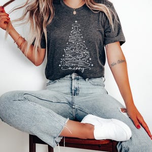 K&ouml;nnte beinhalten: Dunkelgraues T-Shirt mit einem wei&szlig;en Hai-Design in Form eines Weihnachtsbaums. Das Wort "merry" steht darunter. Das T-Shirt besteht aus weichem Material. Ein l&auml;ssiges, festliches Oberteil.