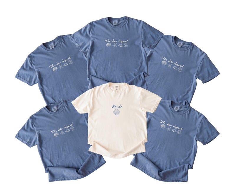 May include: Five blue t-shirts and one white t-shirt. The blue shirts feature the text "The Sea Squad" in white with small shell and starfish graphics. The white shirt features the text "Bride" in blue with a single shell graphic below it.