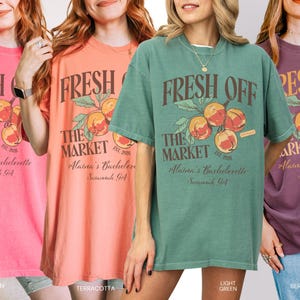 May include: Four women wearing oversized t-shirts in watermelon, terracotta, light green, and berry colors. Each shirt features a graphic with peaches and the text "FRESH OFF THE MARKET" and "Alaina's Bachelorette Savannah, GA."