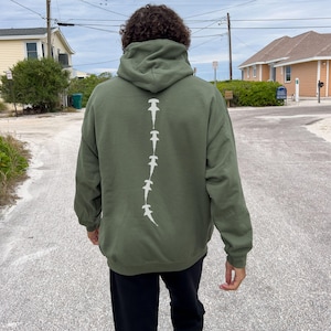 May include: A dark green hooded sweatshirt with a white graphic of a line of hammerhead sharks down the back.