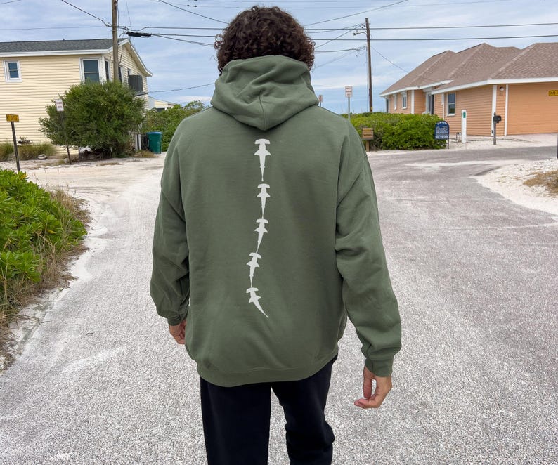 May include: A dark green hooded sweatshirt with a white graphic of a line of hammerhead sharks down the back.