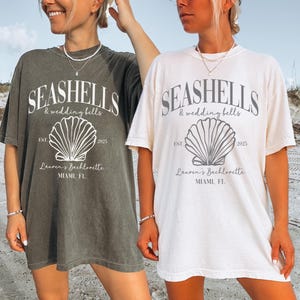 May include: Two women wearing oversized t-shirts with a seashell graphic and the text "Seashells & wedding bells" and "Lauren's Bachelorette Miami, FL".