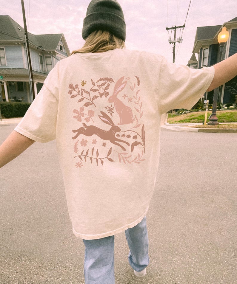 Pu&ograve; includere: Una t-shirt color crema con un design floreale rosa con due conigli e foglie. Il design &egrave; sul retro della t-shirt.