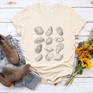 May include: A beige t-shirt with a graphic print of multiple oysters in black and white.