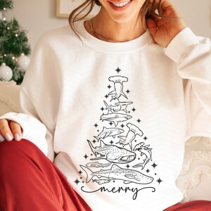 K&ouml;nnte beinhalten: Wei&szlig;es Sweatshirt mit einem schwarzen Strichzeichnungen-Weihnachtsbaum aus verschiedenen Haiarten. Das Wort "merry" ist unten in Schreibschrift geschrieben. Ein festliches Design.