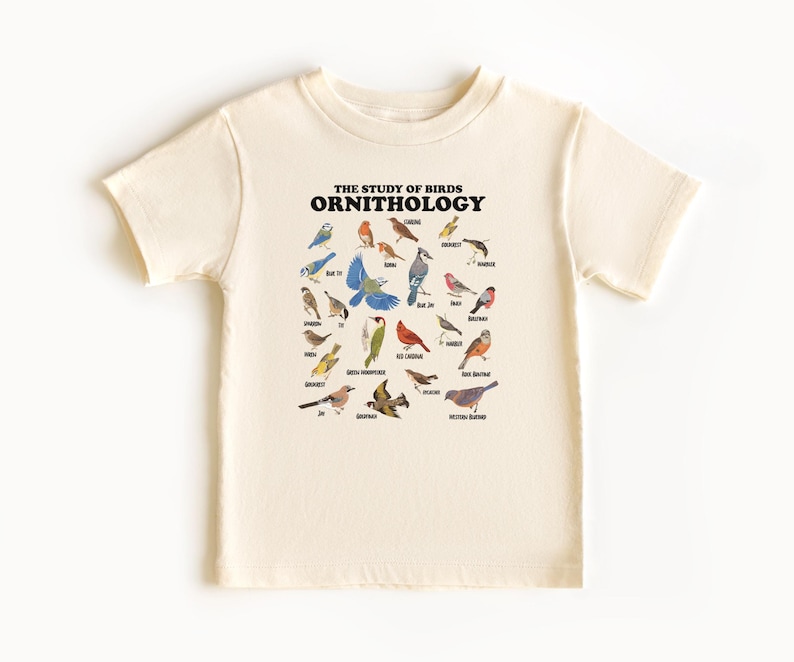 May include: A cream-coloured t-shirt with a graphic of various birds and their names. The text "THE STUDY OF BIRDS ORNITHOLOGY" is printed at the top of the graphic.