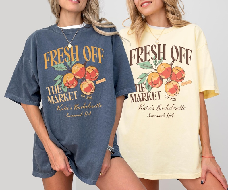 May include: Two oversized t-shirts, one navy blue and one pale yellow, each featuring the text "FRESH OFF THE MARKET" above a graphic of peaches. The text "Katie's Bachelorette Savannah, GA" is printed below the graphic.