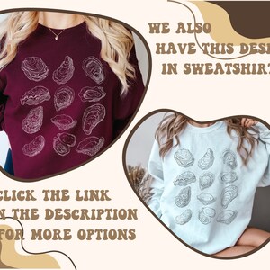 May include: Two women's sweatshirts with a graphic design of oysters. The sweatshirt on the left is maroon and the sweatshirt on the right is light blue. The text "CLICK THE LINK IN THE DESCRIPTION FOR MORE OPTIONS" is at the bottom left of the image. The text "WE ALSO HAVE THIS DESIGN IN SWEATSHIRT" is at the top right of the image.