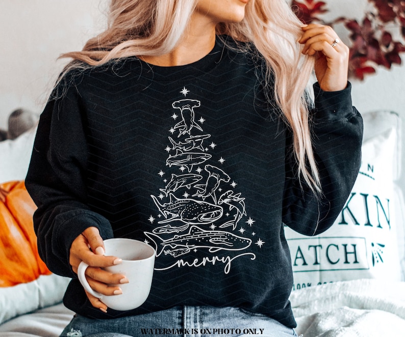 K&ouml;nnte beinhalten: Schwarzes Sweatshirt mit einem wei&szlig;en Design eines Weihnachtsbaums, der aus verschiedenen Haiarten besteht. Das Wort "merry" ist kursiv geschrieben. Das Sweatshirt hat einen Rundhalsausschnitt.