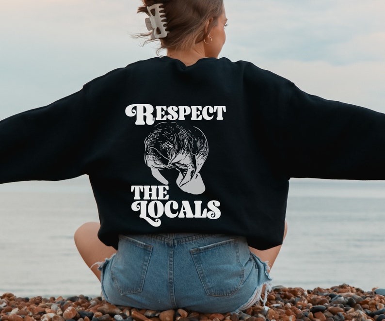 May include: A black sweatshirt with a white graphic print of a manatee and the text "Respect the Locals" in a retro font.