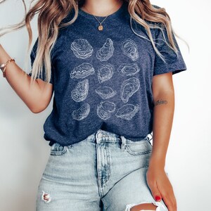 May include: A navy blue t-shirt with a white outline design of multiple oysters. The shirt is made of a soft, comfortable material and has a relaxed fit.
