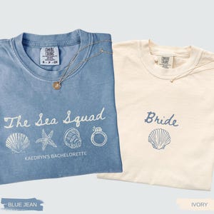 May include: Two short-sleeved crew neck t-shirts. The blue jean shirt features the white text The Sea Squad, Kaedryn's Bachelorette, and graphics of a seashell, starfish, conch, and ring. The ivory shirt features the blue text Bride and a seashell.