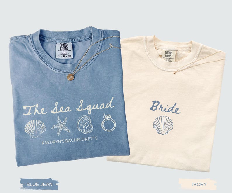 May include: Two short-sleeved crew neck t-shirts. The blue jean shirt features the white text The Sea Squad, Kaedryn's Bachelorette, and graphics of a seashell, starfish, conch, and ring. The ivory shirt features the blue text Bride and a seashell.