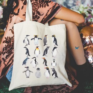 May include: Cream-colored tote bag featuring a collection of watercolor penguin illustrations. The penguins are depicted in various poses and colors, creating a whimsical and artistic design. The bag is made of a sturdy fabric.