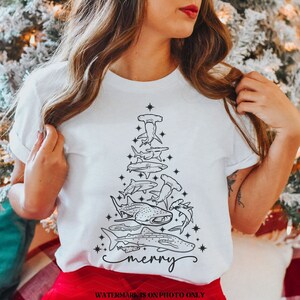 K&ouml;nnte beinhalten: Wei&szlig;es T-Shirt mit einem Weihnachtsbaum-Design aus schwarzen Hai-Illustrationen. Das Wort "merry" ist unten in Schreibschrift geschrieben. Ein einzigartiges festliches Kleidungsst&uuml;ck f&uuml;r die Weihnachtszeit.