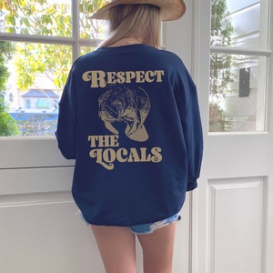 May include: A navy blue sweatshirt with a manatee graphic and the text "Respect the Locals" in a retro font.