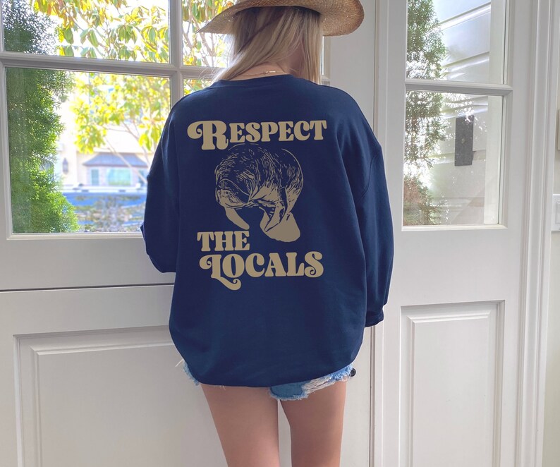 May include: A navy blue sweatshirt with a manatee graphic and the text "Respect the Locals" in a retro font.