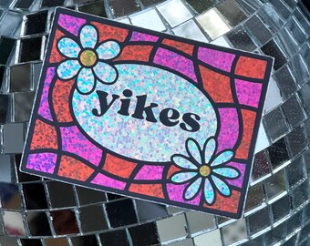 May include: A rectangular sticker with the word "Yikes" in black, surrounded by a colorful design. The design features a glittery oval and two flowers. The background is a disco ball.