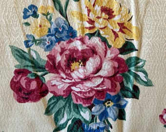 May include: A close-up of a floral fabric with a cream background and a bouquet of pink, yellow, and blue flowers. The flowers are surrounded by green leaves and a blue and white checkered ribbon.