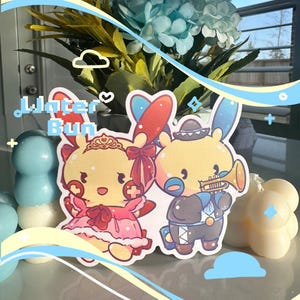 May include: Two cartoon character stickers, one wearing a red and white dress and a crown, the other wearing a blue and black outfit and a sombrero, with the text "Water Bun" above them.