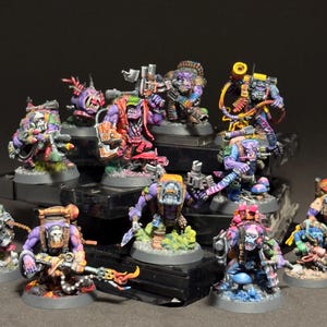 Peut inclure: Ensemble de figurines miniatures de personnages fantastiques, peintes de couleurs vives. Les figurines sont disposées sur une plateforme à plusieurs niveaux, mettant en valeur des armures, des armes et des accessoires détaillés. La palette de couleurs comprend le violet, le vert, le rouge et le bleu.