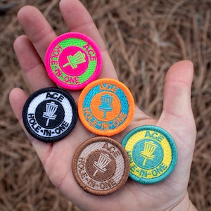 May include: Five embroidered patches with the text "ACE HOLE-IN-ONE" in different colors. The patches are circular and feature a disc golf disc in the center.