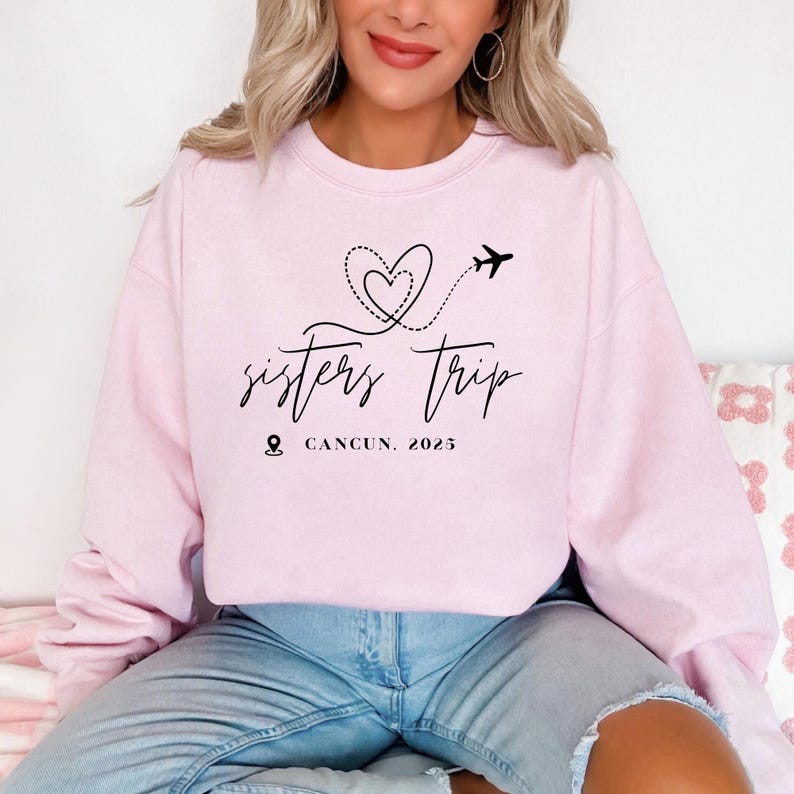 a woman sitting on a bed wearing a pink sweatshirt