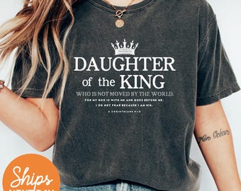 May include: Dark gray unisex t-shirt with the text "DAUGHTER of the KING" and a crown graphic. The shirt also includes a Bible verse. The shirt is made of Comfort Colors material and is available in unisex sizing.
