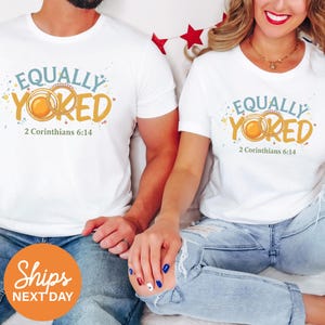 May include: White t-shirts with the text "EQUALLY YOKED" in teal and gold, with the Bible verse 2 Corinthians 6:14. The shirts are worn by two people. The image also includes a "Ships Next Day" sticker.