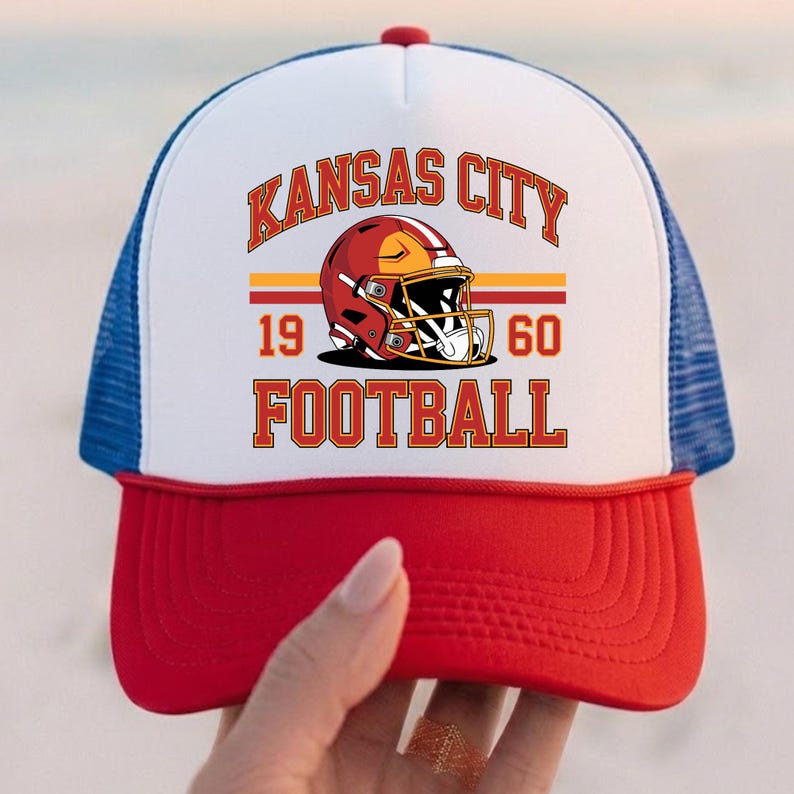 May include: A red, white, and blue trucker hat with the text "Kansas City Football" and a football helmet graphic. The hat has a red peak, a white front panel, and a blue mesh back. The text "1960" is also displayed.