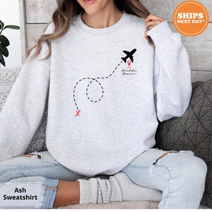 a woman sitting on a couch wearing a sweatshirt with a plane on it