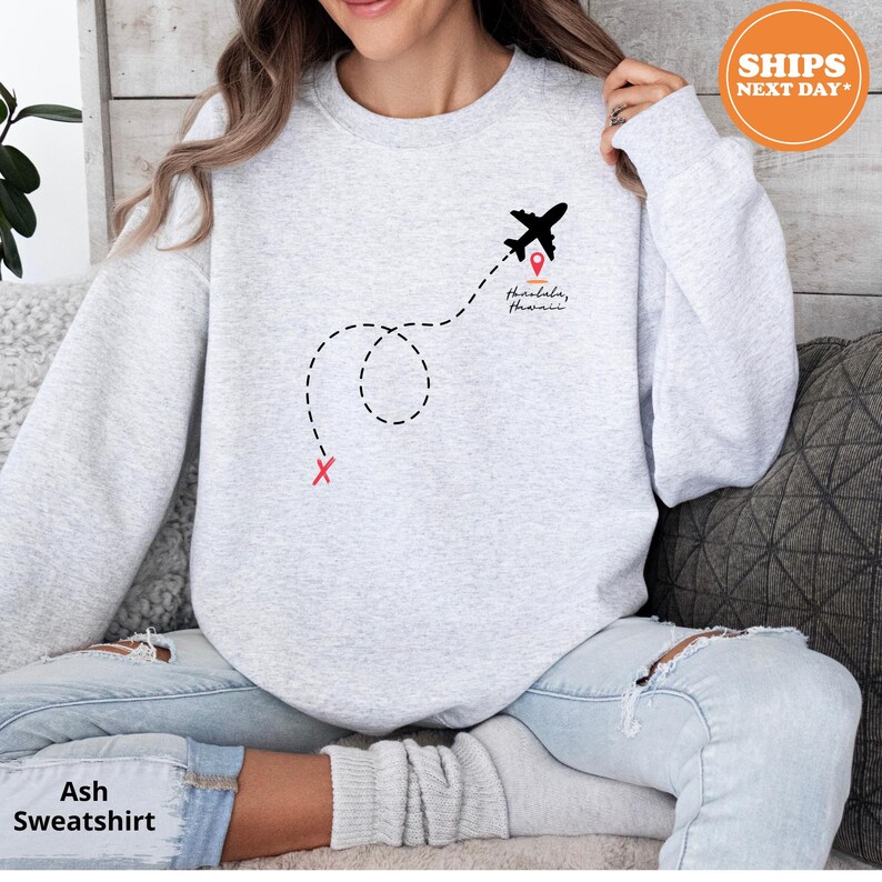 a woman sitting on a couch wearing a sweatshirt with a plane on it